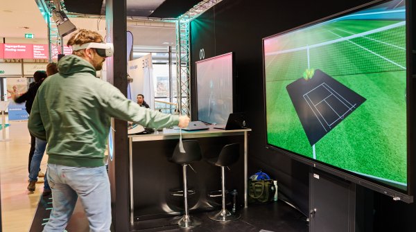 Man wears VR glasses, in the background is a screen with a playing field